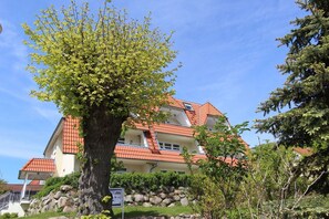 A multi-story building with a red-tiled roof, surrounded by greenery and a large tree.
