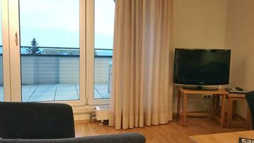 Una sala de estar con televisor sobre un mueble de madera, un sofá y una mesa con control remoto.