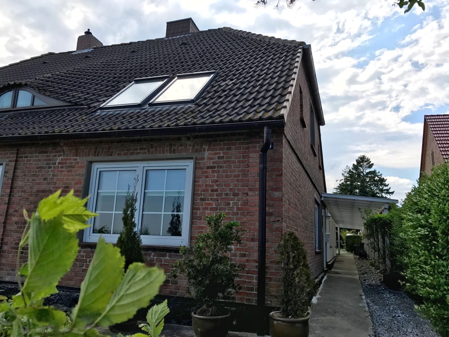 Ein Backsteinhaus mit Ziegeldach, zwei Dachfenstern und einem Weg zu einer überdachten Terrasse.