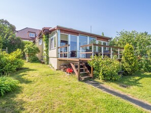 Ein modernes Haus mit großen Glasfenstern, einer Holzterrasse und einem Garten.