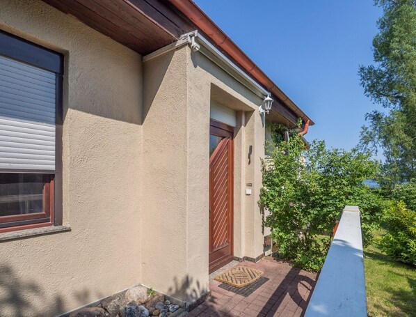 Ein Haus mit hellbeige Fassade, einer Holztür und einem Fenster mit Jalousien.