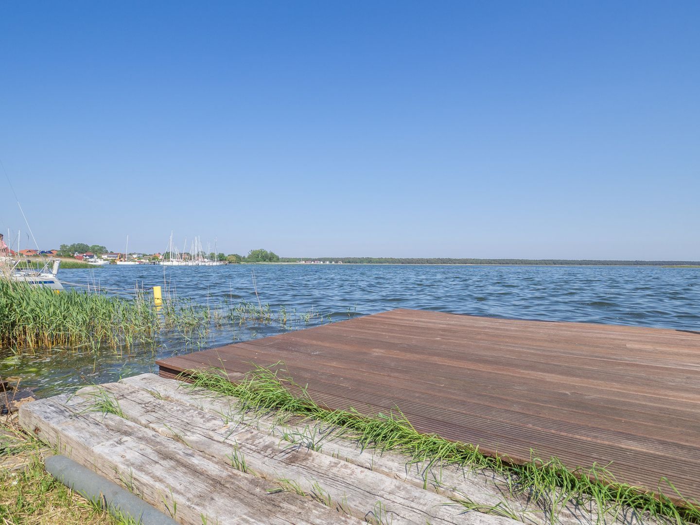 A wooden dock extending into a calm body of water with boats in the background.