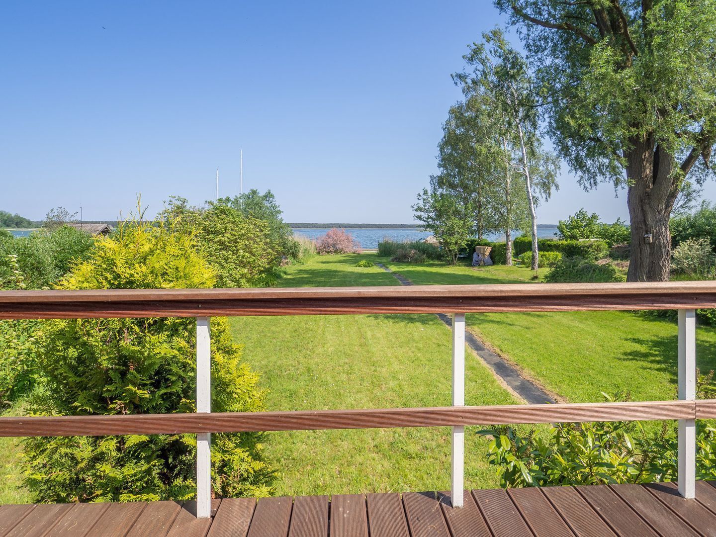 Una terraza de madera con vista a un área verde, árboles y una masa de agua.
