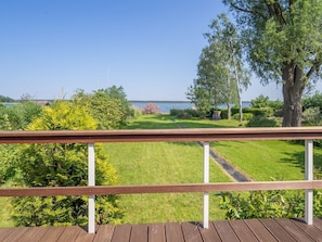 Una terraza de madera con vista a un área verde, árboles y una masa de agua.