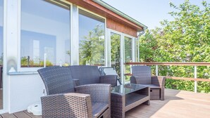 Une terrasse extérieure avec des meubles en osier et de grandes fenêtres.