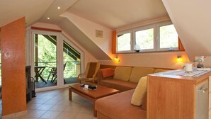 Een gezellige zolderkamer met een bank, een bijzettafeltje en een klein houten bureau. Er is een schuifdeur van glas die leidt naar een terras.