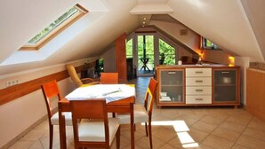 Een eetgedeelte met een tafel en stoelen, een keuken met kastjes, en uitzicht door een glazen deur op een buitenruimte.