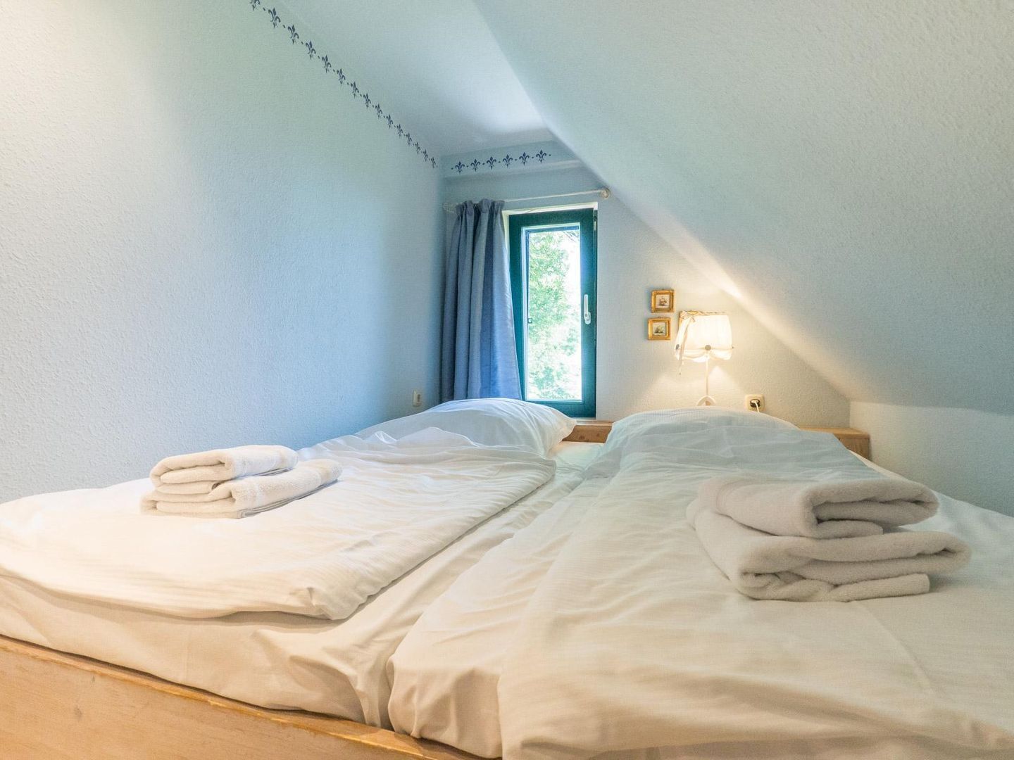 A bedroom with two beds, a window with curtains, a bedside lamp, and a wall with a decorative border.