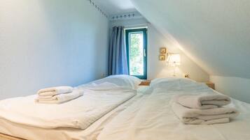 A bedroom with two beds, a window with curtains, a bedside lamp, and a wall with a decorative border.
