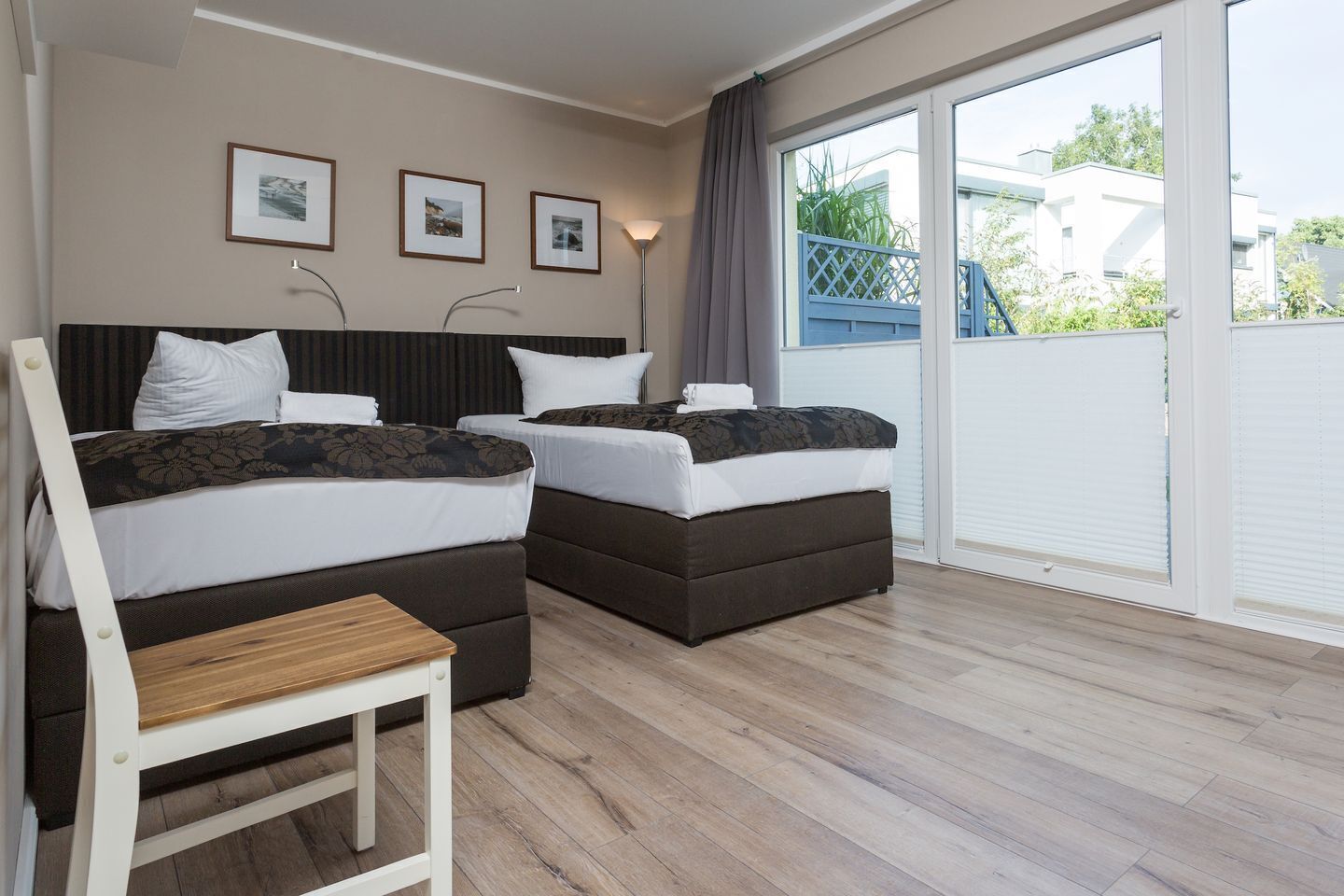 A hotel room with two beds, a wooden chair, and a large sliding glass door to the outside.