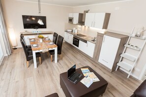 Una cucina moderna con mobili bianchi, un forno a microonde e una lavastoviglie. C'è un tavolo da pranzo con sedie e un portatile sul tavolo.