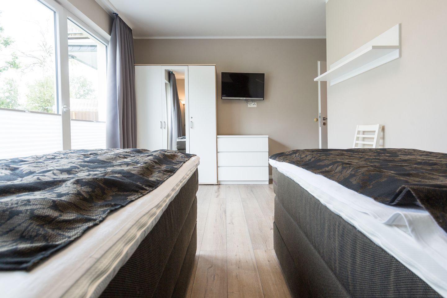 A bedroom with two beds, a TV, a wardrobe, and a desk.
