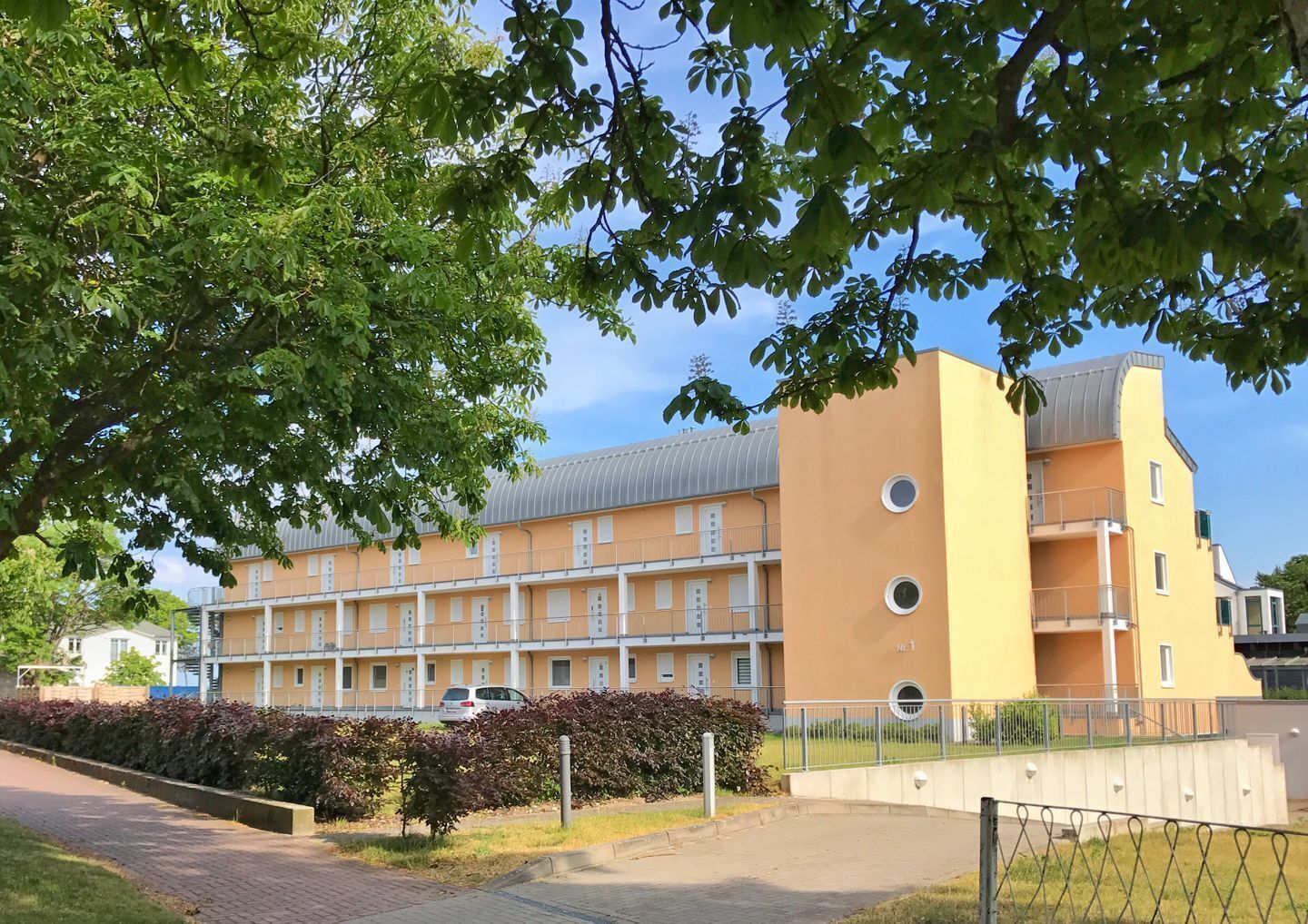 Un edificio a più piani con facciata gialla, balconi e un'area di parcheggio.