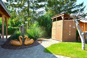 A wooden shed with a slanted roof, a paved pathway leading to it, and two swan sculptures in the foreground. - "Lütt Eiland" Vacation Home (Glowe)