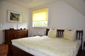 A bedroom with a bed, a wooden dresser, a radiator, a window with a yellow blind, and a framed picture on the wall.