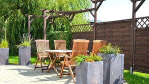 An outdoor patio with a wooden pergola, a table with chairs, and planters with greenery. - Vacation home "Lütt Eiland" (Glowe)