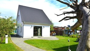 A small, single-story house with a tiled roof, a paved driveway, and a well-maintained lawn. - Vacation home "Lütt Eiland" (Glowe)