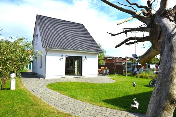 A small, single-story house with a tiled roof, a paved driveway, and a well-maintained lawn.