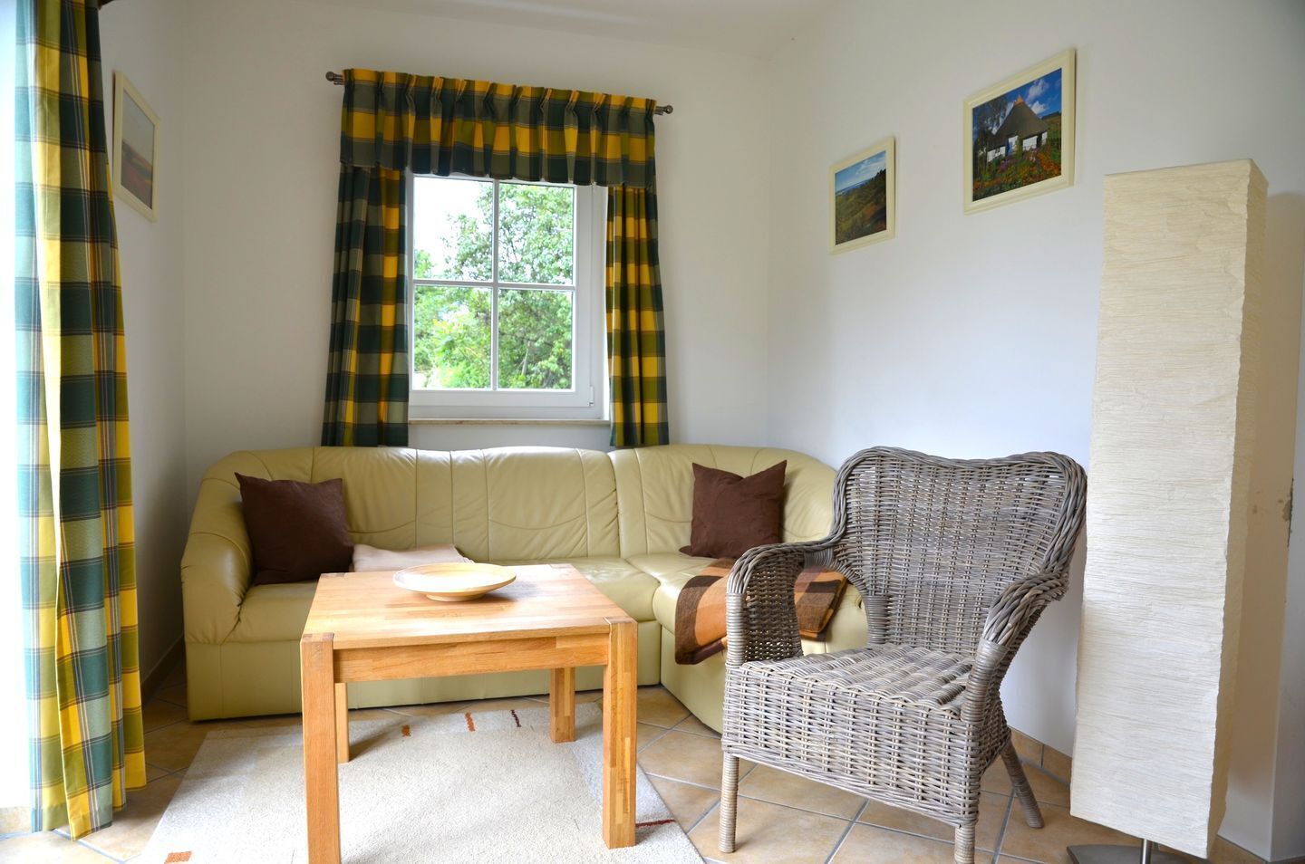A cozy living room with a sofa, a wicker chair, a wooden table, and a window with curtains.
