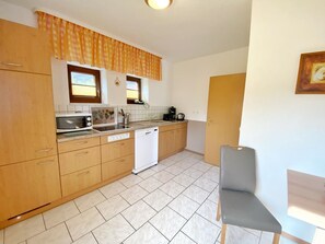 A compact kitchen with wooden cabinets, a white dishwasher, and a small dining area with a grey chair.