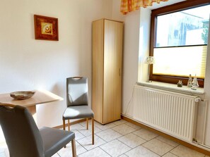 A small room with a table, two chairs, a tall wardrobe, a window with a view, and a radiator.