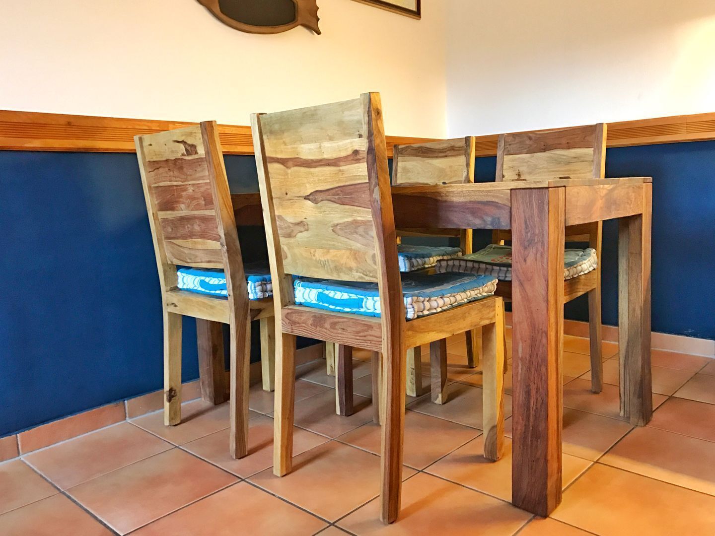 Un coin repas comprenant quatre chaises en bois et une table, chaque chaise étant agrémentée d’un coussin à motifs bleus et blancs.