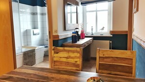 A compact kitchen with a wooden table, chairs, and a small island. There is a window with a view of the outside, a radiator, and a mirror above the island.