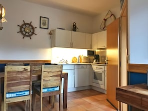 A compact kitchen with white cabinets, a microwave, a coffee maker, and a sink. There are two wooden chairs with blue cushions.