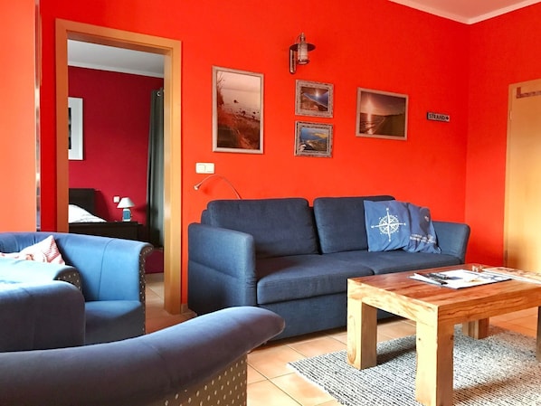A living room with a blue sofa, a wooden coffee table, and a red accent wall.