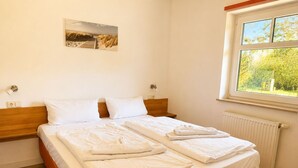 A bedroom with a bed, a window with a view, a radiator, and a painting on the wall. - Vacation home Emma - Apartment 2 (Lohme)