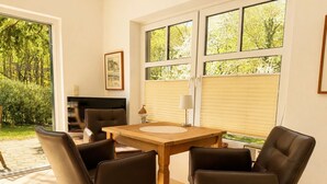 A dining area with a wooden table and four chairs, a television, and a window with blinds. - Vacation home Emma - Apartment 2 (Lohme)