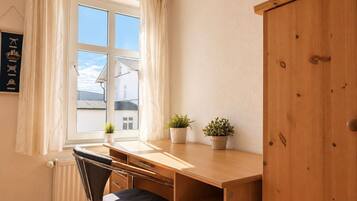Ein Zimmer mit Schreibtisch, Stuhl, Heizkörper, einem Fenster mit Vorhängen und einem Schrank aus Holz.