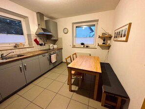 A compact kitchen with grey cabinets, a wooden table, and a window overlooking a building. - Holiday home Boddenperle in Glowe - Holiday home "Boddenperle" (Glowe)