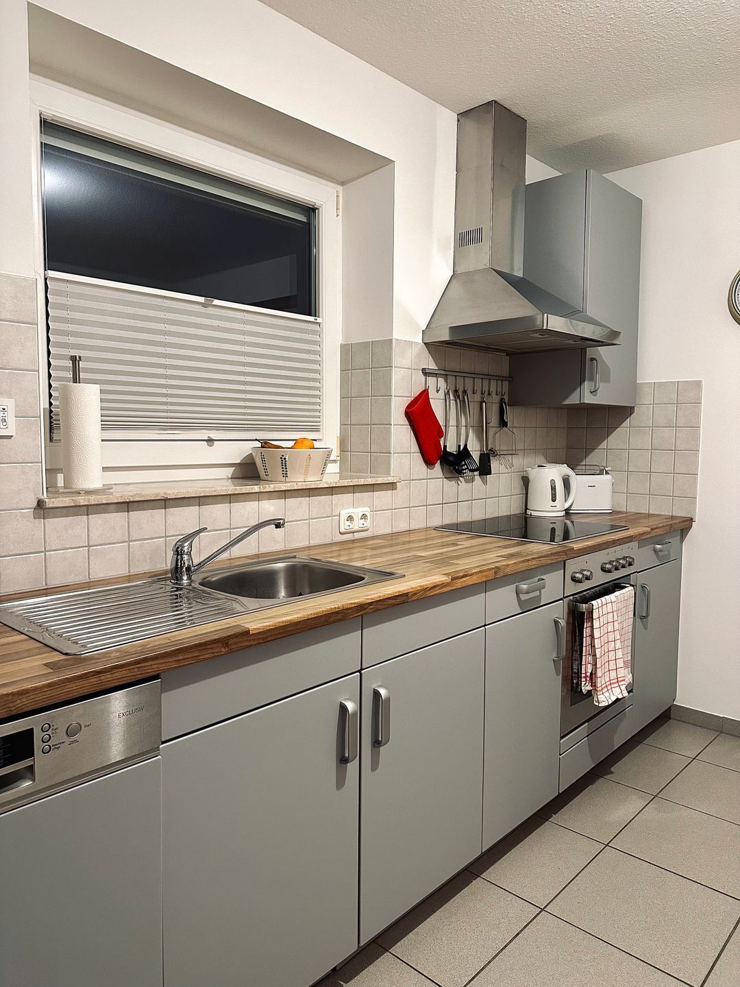 A modern kitchen with a wooden countertop, stainless steel sink, and grey cabinets.
