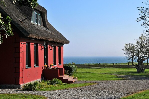 A red building with a thatched roof, a gravel path, and a view of the sea.