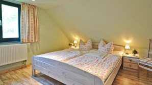 Quarto com cama de madeira, duas mesas de cabeceira com abajures, um radiador e uma janela com cortinas.