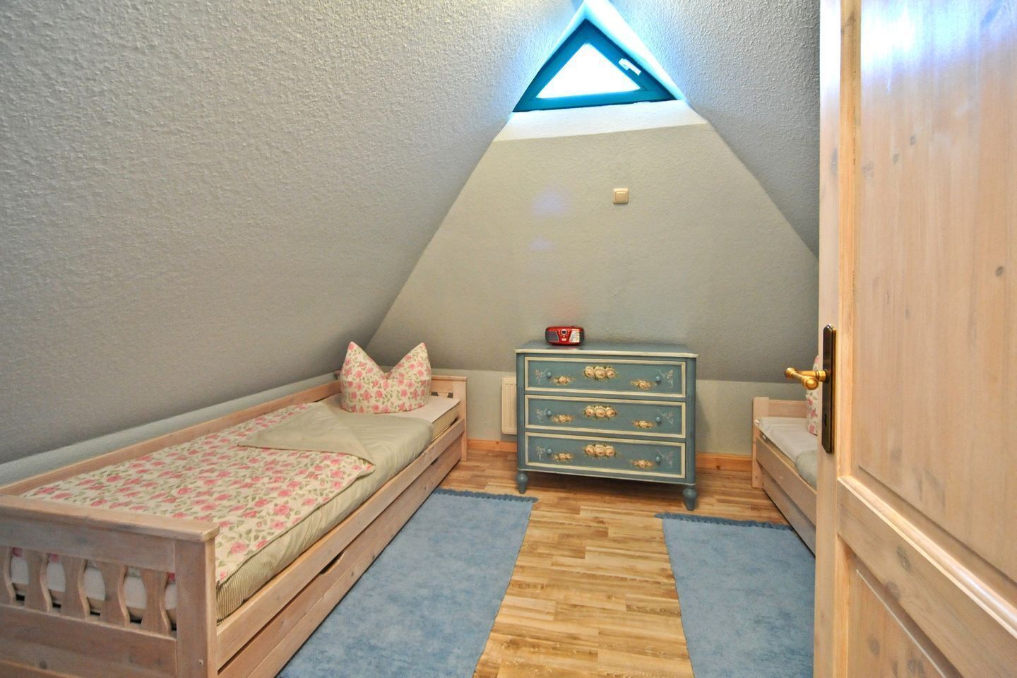 A small bedroom with a sloped ceiling, a wooden bed, a dresser, and a small table.