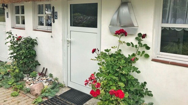 A white house with a thatched roof, a white door, and a window with a metal awning. - Doppelhaushälfte Nr. 2 im Feriengarten (Nardevitz auf Rügen)