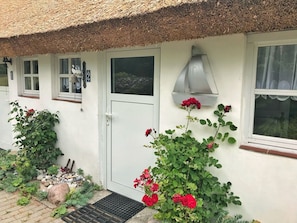 Een wit huis met rieten dak, een witte deur en een raam met een metalen luifel.