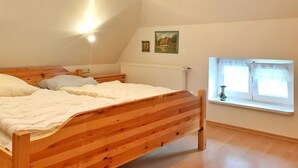 A bedroom with a wooden bed, a radiator, a window with curtains, and a picture on the wall. - Doppelhaushälfte Nr. 2 im Feriengarten (Nardevitz auf Rügen)
