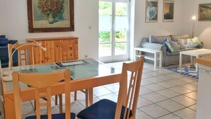 A dining area with a glass table, wooden chairs, and a wooden cabinet. There is a sofa and a coffee table in the living area. - Doppelhaushälfte Nr. 2 im Feriengarten (Nardevitz auf Rügen)