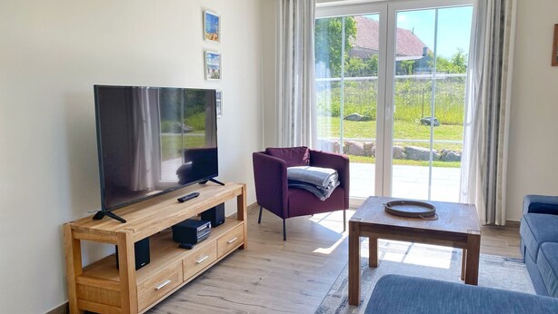 Moderni olohuone, jossa on litteänäyttöinen televisio puisen jalustan päällä, violetti nojatuoli, sininen sohva ja pieni pöytä, jonka päällä on tarjotinalusta.