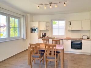 Een moderne keuken met witte kasten, een houten eettafel met vier stoelen, een inbouwoven en een raam dat voor natuurlijk licht zorgt.