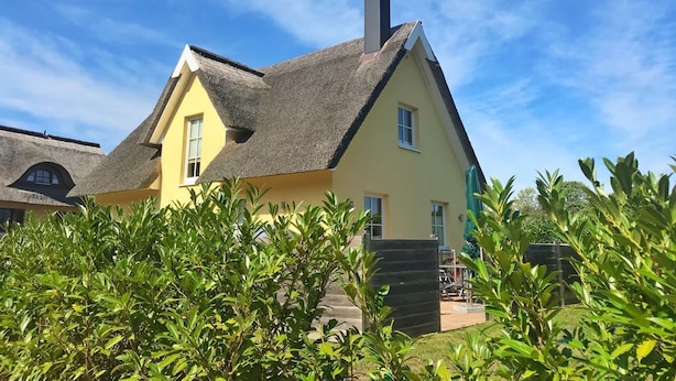 A yellow house with a thatched roof, surrounded by greenery.