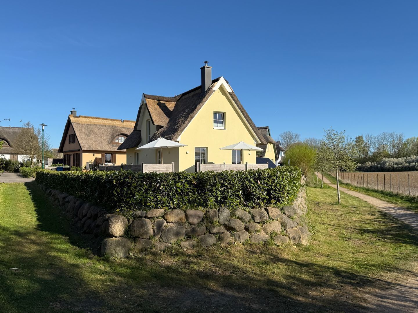 A yellow house with a stone wall in front, a thatched roof, and a clear blue sky.
