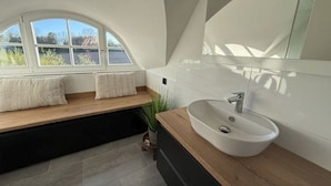 A modern bathroom with a large window, a white sink, and a wooden bench.