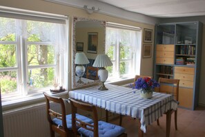A dining room with a checkered tablecloth, two chairs, a vase with flowers, a bookshelf, and a large mirror with a decorative frame.