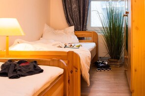 A cozy room with a wooden bed, a bedside table with a lamp, a small plant, and a shoe rack. - Dünenresidenz - Apartment 13 "Sandburg" (Breege)