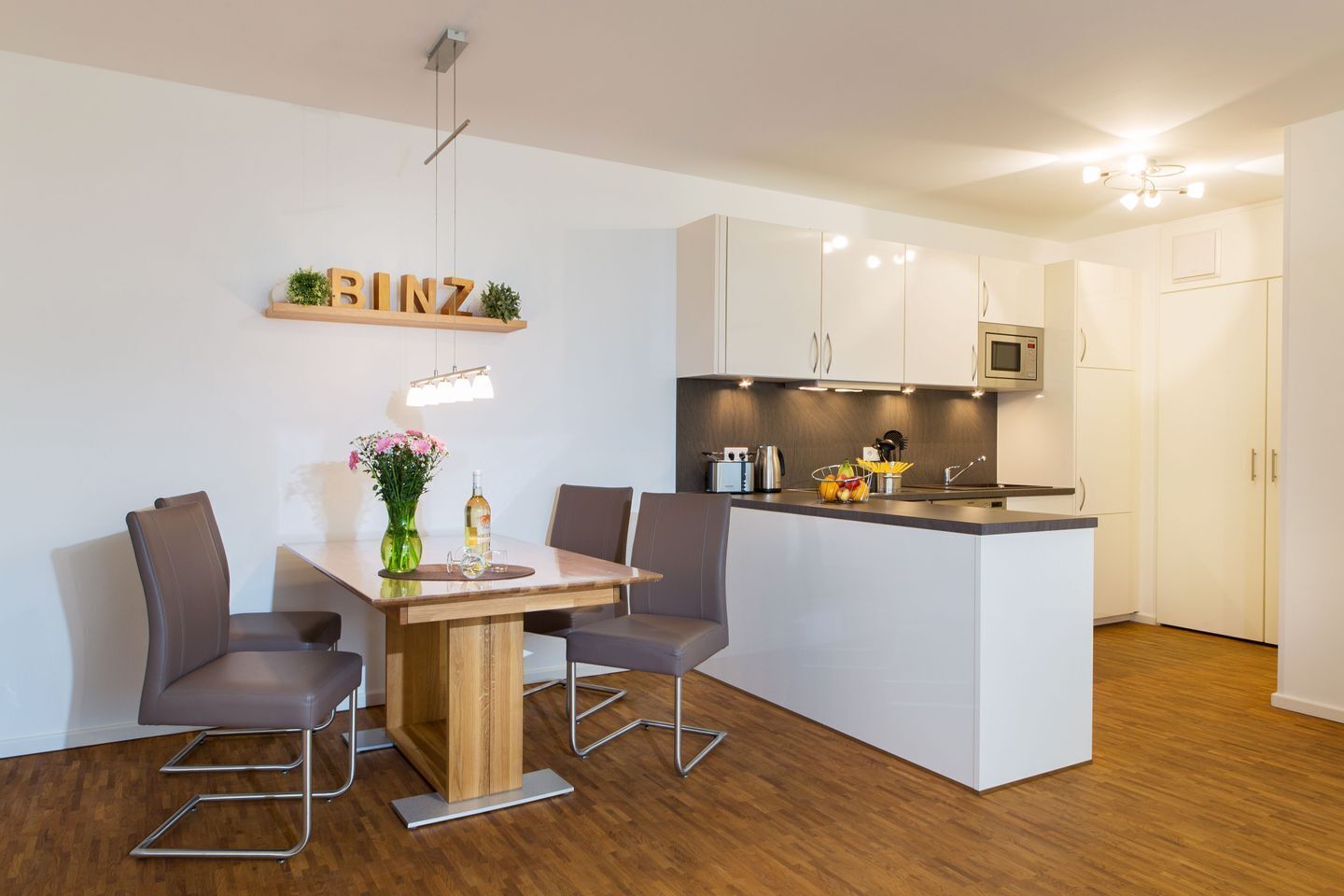 Eine moderne Küche mit weißen Schränken, einer zentralen Kochinsel und einem Essbereich mit einem Holztisch und zwei Stühlen.