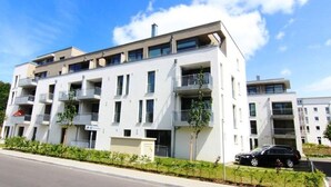 A modern multi-story residential building with balconies, a parking area, and a clear sky. - Dünenresort Binz - Apartment 4.1.6 (Binz)